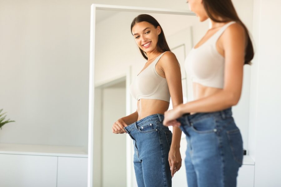 Excited young fit woman losing weight and wearing old too big jeans - weight loss injections