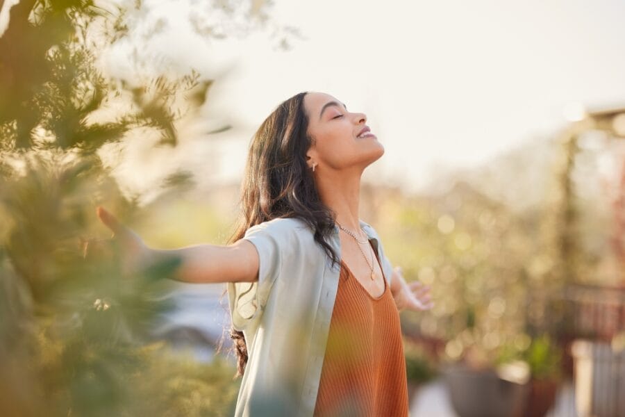 A young woman with arms outstretched enjoys the sunlight and fresh air outdoors. - Sick Visit