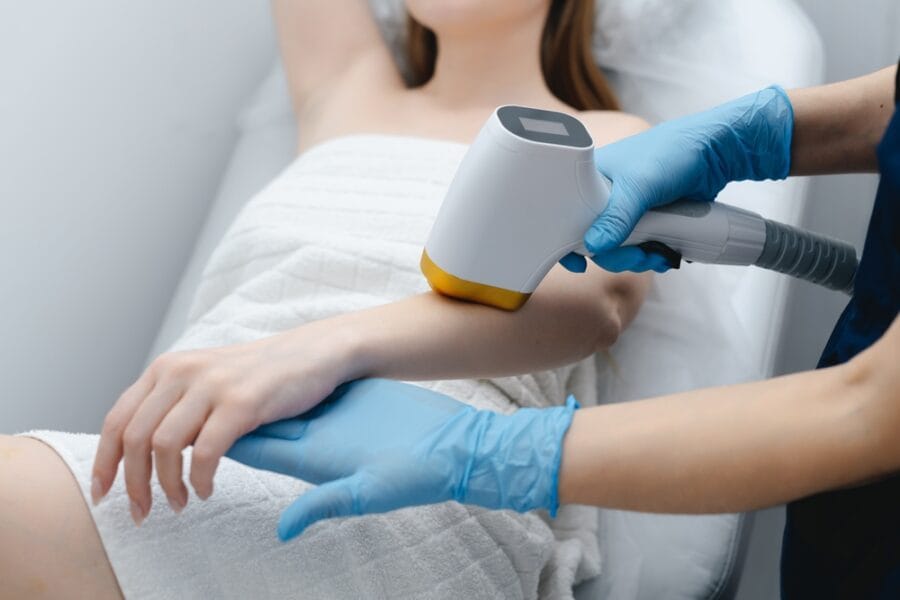 A specialist wearing blue gloves performs a laser therapy treatment on a woman's arm. - Laser Therapy